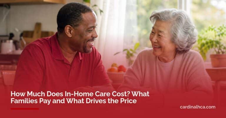 A smiling caregiver and an older woman share tea at a sunny kitchen table at home.